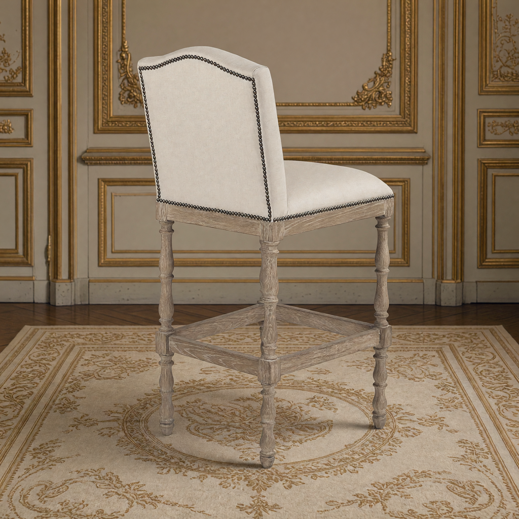 Aria French Turned Oak Bar Stool in Natural Linen, Recycled Oak, rear three-quarter view showing the nailhead trim, in a French salon