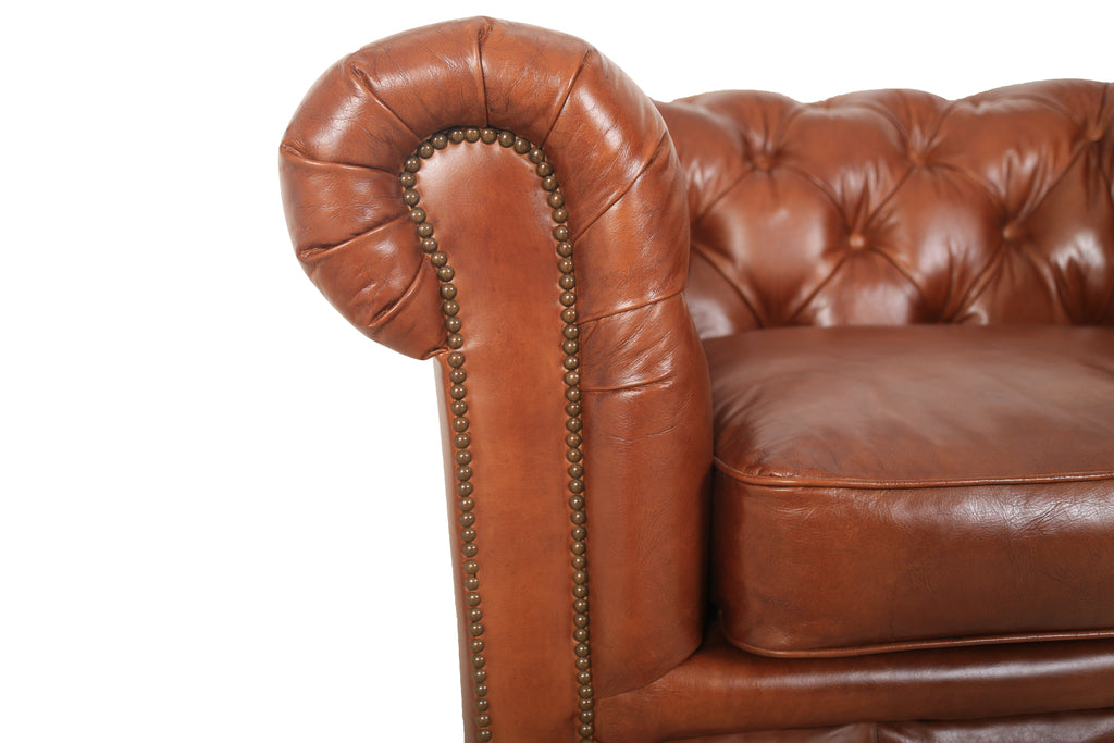 Close-up of the Arthur arm chair's rolled arm, tufting and nailhead trim in cognac leather