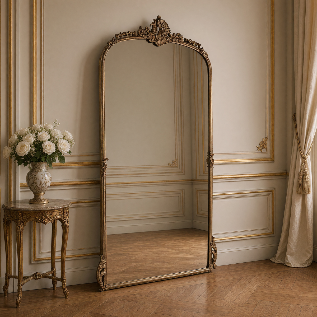 Godric French gilded metal arch floor mirror, styled on parquet with a gilded side table and white roses