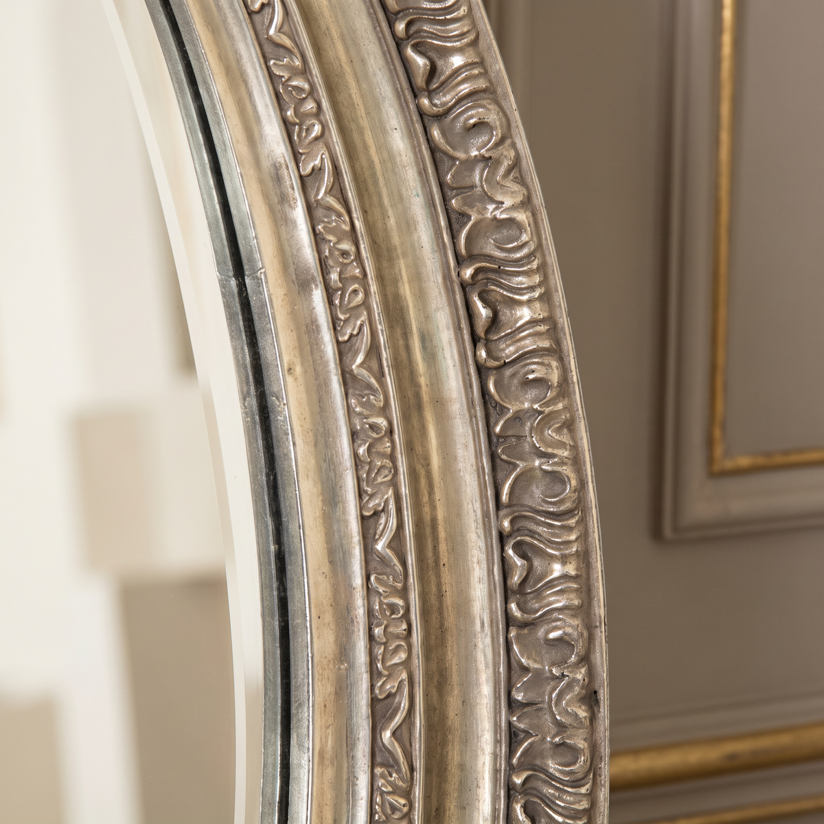 Detail of the antiqued relief border and beveled glass of the Mael round mirror in silver-gold