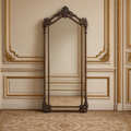 Aurelia ornate iron floor mirror in antiqued bronze-brown leaning on a gilded ivory boiserie wall over an antique Aubusson carpet