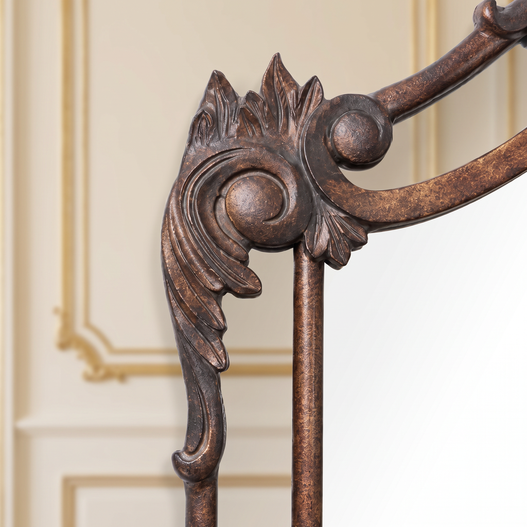 Detail of the sculpted acanthus scroll and leaf crest of the Aurelia floor mirror in antiqued bronze-brown